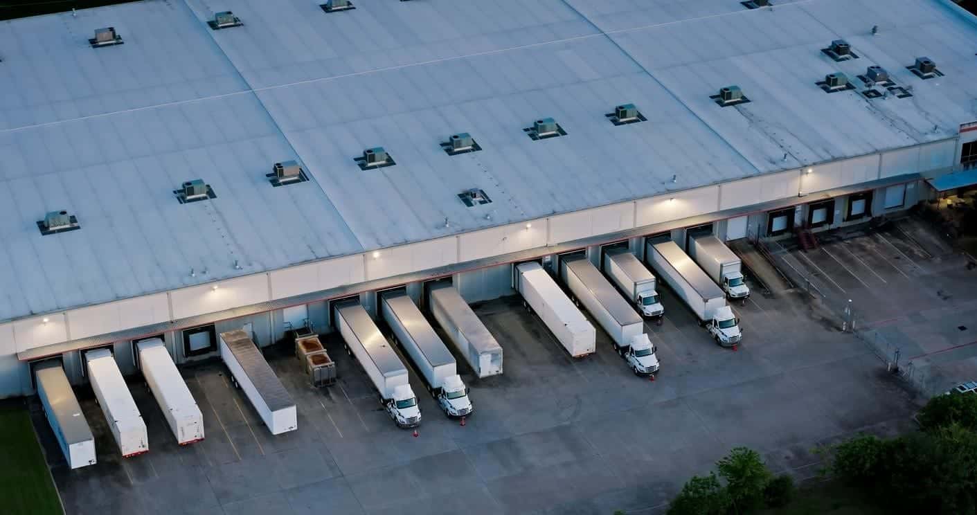 Aerial shot of large semi-trucks parked in a warehouse in the evening.