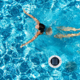 A person is swimming next to a solar pool ionizer.