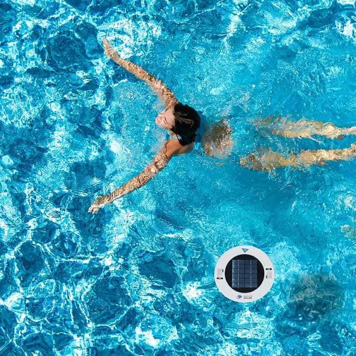 A person is swimming next to a solar pool ionizer.