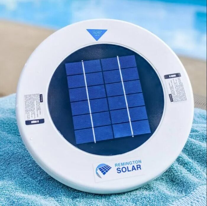 A close-up of a Remington Solar Sun-Shock pool ionizer with blue solar panels, resting on a turquoise towel beside a pool.