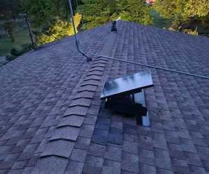 Side view of a Remington Solar attic fan on a roof with trees in the background.
