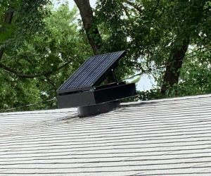 Remington Solar attic fan in a roof with trees in the background.