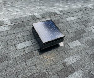 The top of a Remington Solar attic fan on a gray, shingled roof.