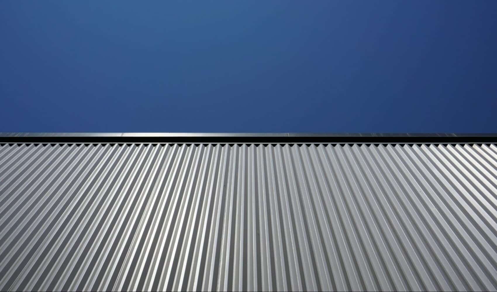 Close-up view of a modern corrugated metal wall set against a clear blue sky.