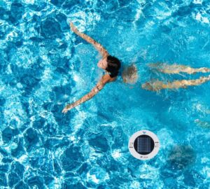 A person swimming in a pool next to a Remington Solar Pool Ionizer.